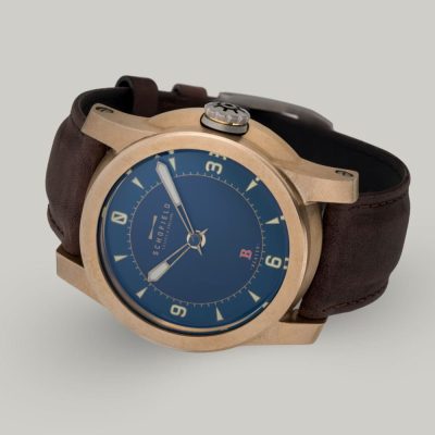 The B3 ✦ Raw Bronze wristwatch with a raw bronze case, blue dial, and tan hour markers with a numerals at 3,6,9 and 12. A small Sign-of-Life seconds hand can be seen in the centre.