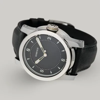 Polished watch with Black Dial. Schofield silver treasure A Treasure Watch ✦ Silver with a stainless steel case and a black leather strap. It features a black dial with white hour markers and hands, along with a crown engraved with a wheel design. Schofield is displayed on the minimal dial.