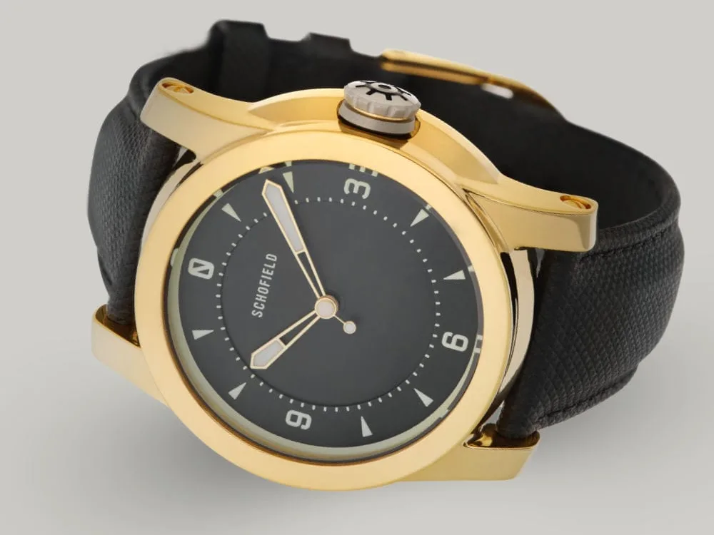 A polished gold-plated Treasure Watch ✦ Gold with a black leather strap. This treasure watch features a black minimal dial with Super-LumiNova markings and hands, including numerals at 3, 6, 9, and 12.