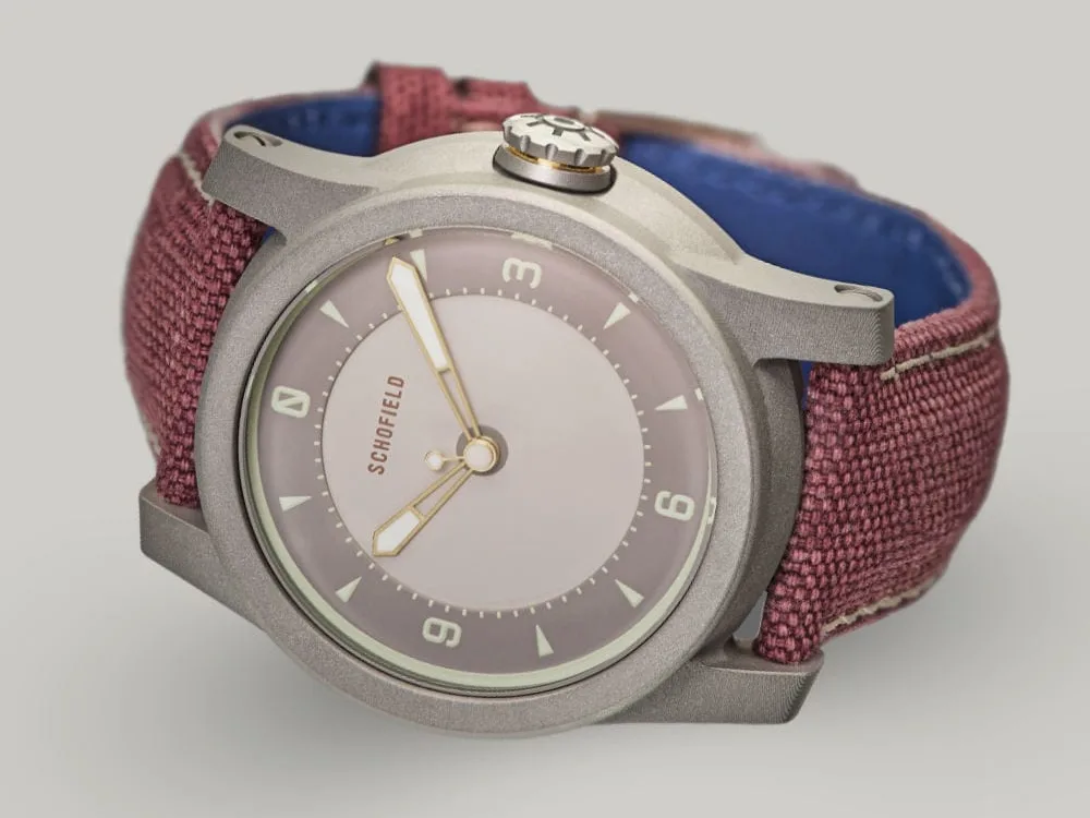 The B5 ✦ Japanese Sakura wristwatch with a metal case and purple-red fabric strap, reminiscent of Japanese Sakura blossoms. The minimalistic watch face features a light grey dial, simple hour markers, and the brand name "Schofield" at the top.