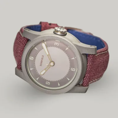 Japanese Watches by Schofield, the B5 Sakura The B5 ✦ Japanese Sakura wristwatch with a metal case and purple-red fabric strap, reminiscent of Japanese Sakura blossoms. The minimalistic watch face features a light grey dial, simple hour markers, and the brand name "Schofield" at the top.