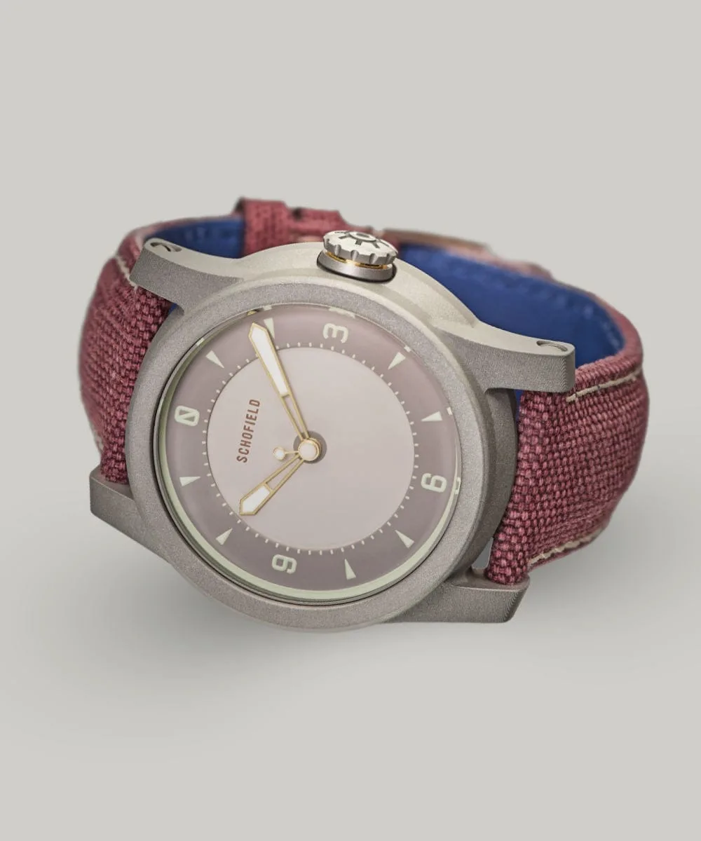 The B5 ✦ Japanese Sakura wristwatch with a metal case and purple-red fabric strap, reminiscent of Japanese Sakura blossoms. The minimalistic watch face features a light grey dial, simple hour markers, and the brand name "Schofield" at the top.