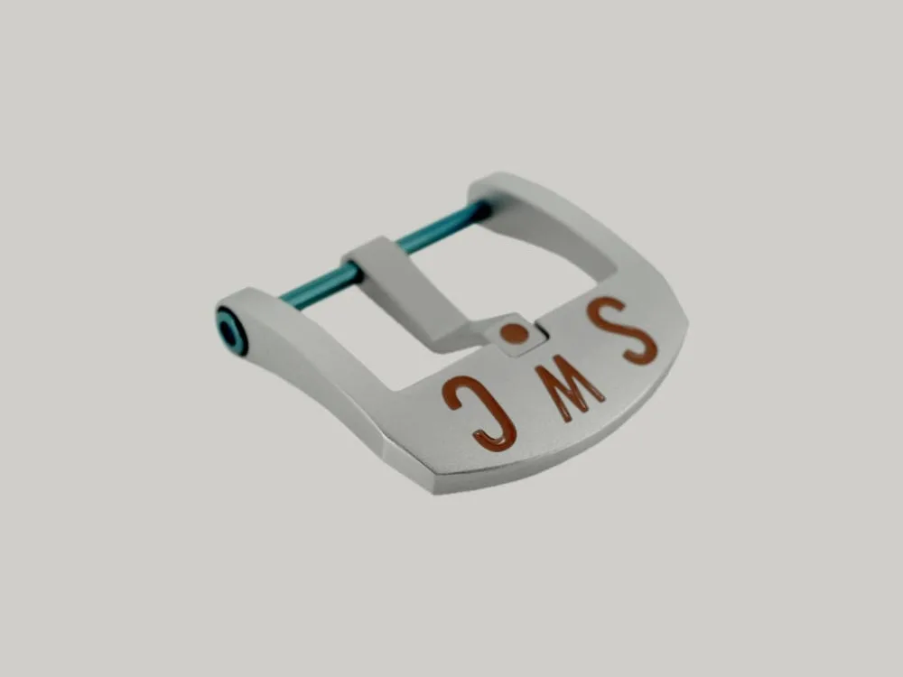 A Brushed BE Buckle with a rectangular frame and blue PVD strap fitting screw. The thumbnail style buckle, called The Best Ever Buckle, features the engraved letters "SWC" in a red paint fill.
