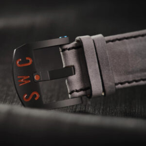 Close-up image of a black buckle on a grey cloud leather watch strap with the letters "SWC" engraved in red on the DLC metal buckle.