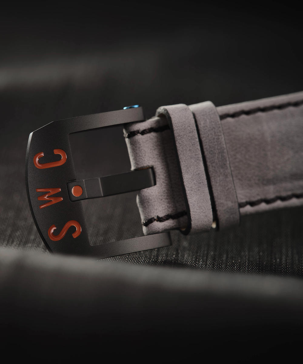 Close-up image of a black buckle on a grey cloud leather watch strap with the letters "SWC" engraved in red on the DLC metal buckle.