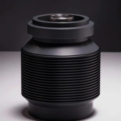 A modern, cylindrical black canister features multiple horizontal ridges and a smooth, flat top with a circular metallic component at the center. The dark background enhances the canister's sleek, industrial design.