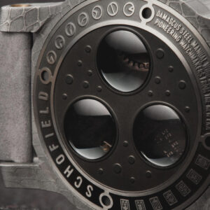 Close-up of a luxury wristwatch showcasing a round, textured, matte grey case with three large circular windows on the back. Engraved text on the caseback rim includes "DAMASCUS STEEL" and "PIONEERING WATCHMAKING".