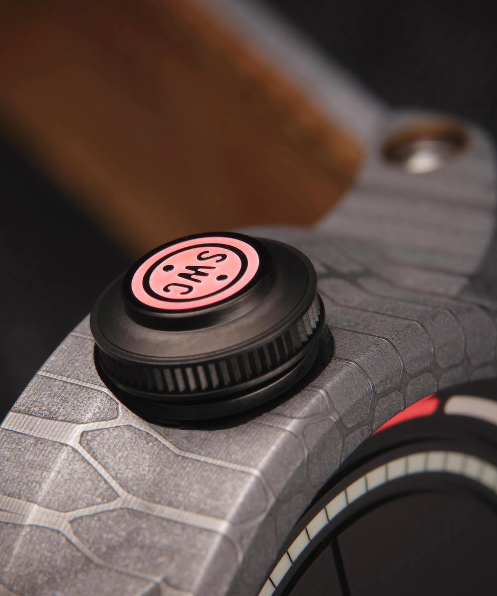 Close-up image of the Obscura watch crown with a textured Black DLC surface and a red circular filled cap labeled “SWC”.