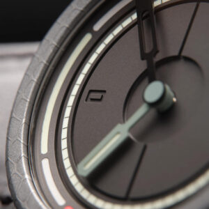 Close-up of a British-made modern analog wristwatch with a dark face. The watch features thick, stylized hands and luminous hour markers.