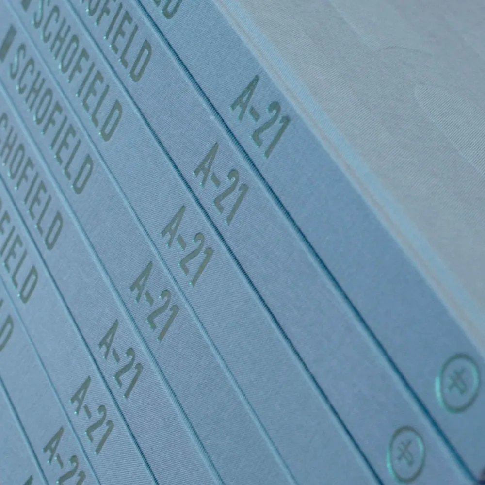 Close-up of a stack of blue/green hard cover books titled "A-21" with the name Schofield on the spine, books containing the intrigue found in the Six Pips newsletter.
