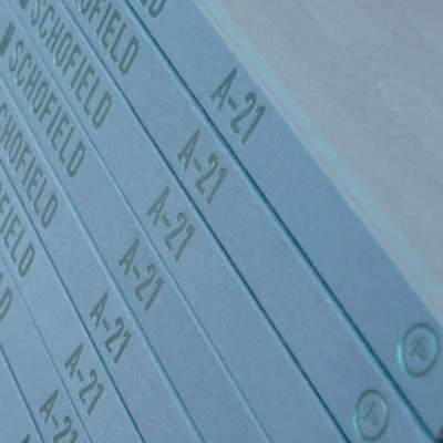Close-up of a stack of blue/green hard cover books titled "A-21" with the name Schofield on the spine, books containing the intrigue found in the Six Pips newsletter.