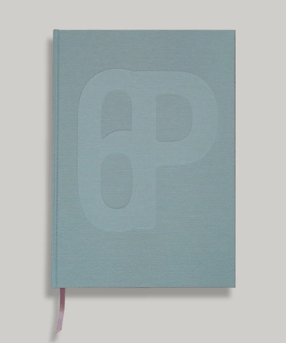 A light blue/green hardcover copy of Almanac ✦ 21 with an embossed abstract '6p' design and a pink ribbon bookmark.