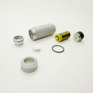 The components of the Ultra Violet Torch are arranged on a plain surface, featuring a silver metal case, lens, reflector, battery, and rubber gasket. The parts are scattered with the focus on the silver torch case in the foreground.