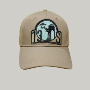 A BAD MOOD CAP in beige showcases a circular patch adorned with a stylized figure, the number 130S, and abstract black and teal designs. The cap is set against a simple light gray background, enhancing its minimalist appeal.