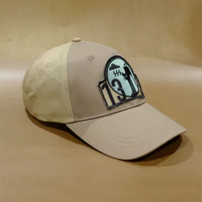 2024 PRODUCT TEMPLATE A "BAD MOOD CAP" in beige, featuring an embroidered patch with the number 13 and a silhouette of a baseball player, set against crossed bats, placed on a textured brown surface.