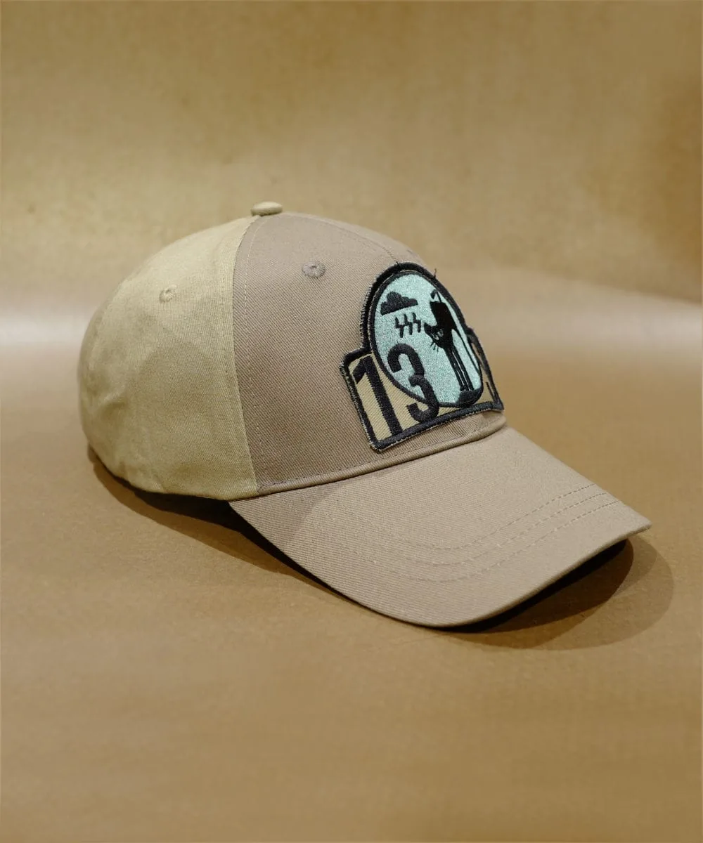 2024 PRODUCT TEMPLATE A "BAD MOOD CAP" in beige, featuring an embroidered patch with the number 13 and a silhouette of a baseball player, set against crossed bats, placed on a textured brown surface.