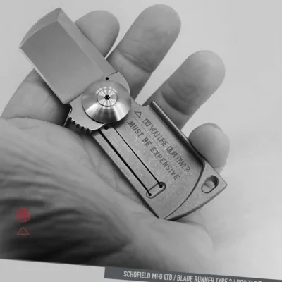 A hand holds a compact, rectangular folding knife labeled “MUST BE EXPENSIVE.” The knife has an industrial design and engraved details. The image is in black and white with graphic elements and text at the bottom.