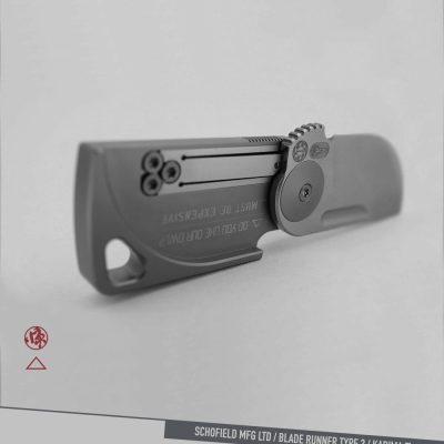 A sleek, grey folding knife with a minimalist design, unfolded on a grey surface. Branding and labels are visible, including “BLADE RUNNER TYPE 3 / KADIMA Ti” at the bottom.