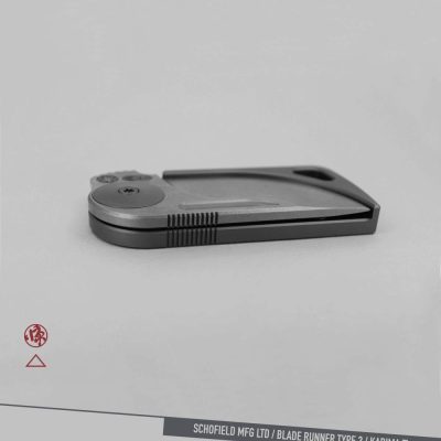 A sleek, modern folding knife with a metallic finish is displayed closed on a light gray background. The text at the bottom reads "SCHOFIELD MFG LTD / BLADE RUNNER TYPE 3 / KADIMA Ti.