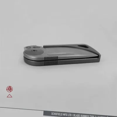 A sleek, modern folding knife with a metallic finish is displayed closed on a light gray background. The text at the bottom reads "SCHOFIELD MFG LTD / BLADE RUNNER TYPE 3 / KADIMA Ti.