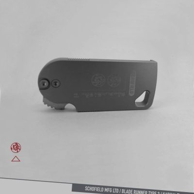 A compact, foldable utility knife with a gray metal body lies on a light surface. The words "SCHOFIELD MFG LTD / BLADE RUNNER TYPE 3 / KADIMA Ti" are printed along the bottom edge of the image.