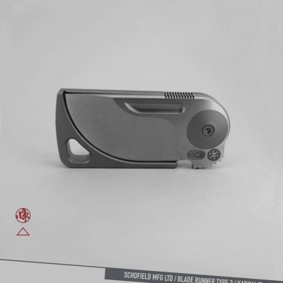 A sleek, modern folding knife with a minimalist design is shown closed against a gray background. The text at the bottom reads "SCHOFIELD MFG LTD / BLADE RUNNER TYPE 3 / KADIMA Ti.