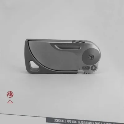 A sleek, modern folding knife with a minimalist design is shown closed against a gray background. The text at the bottom reads "SCHOFIELD MFG LTD / BLADE RUNNER TYPE 3 / KADIMA Ti.