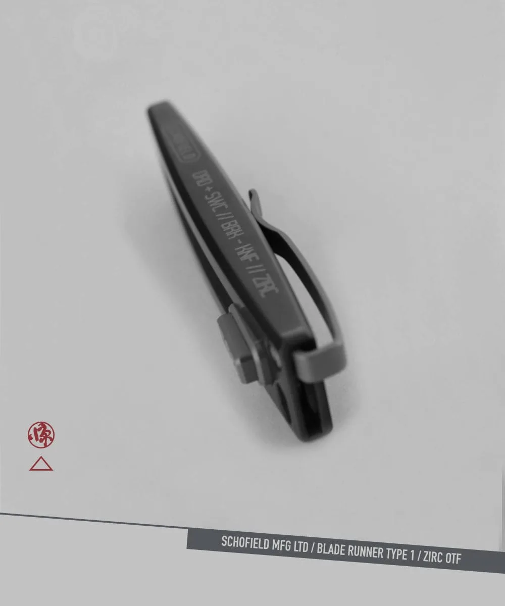 A dark metallic clip with engraved text rests on a light gray surface. Nearby are a small red logo and a label reading "SCHOFIELD MFG LTD / BLADE RUNNER TYPE 1 / ZIRC OTF.