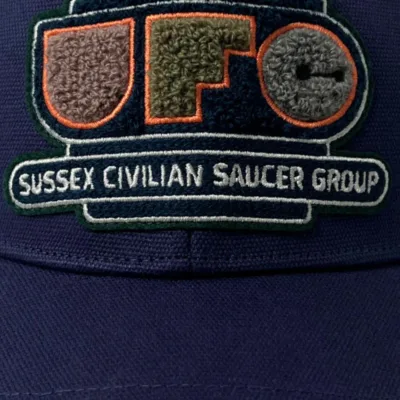 SCHOFIELD UFO PATCH CAP PATCH MAIN An indigo cap with chenille patch reading UFO Sussex Civilian Saucer Group