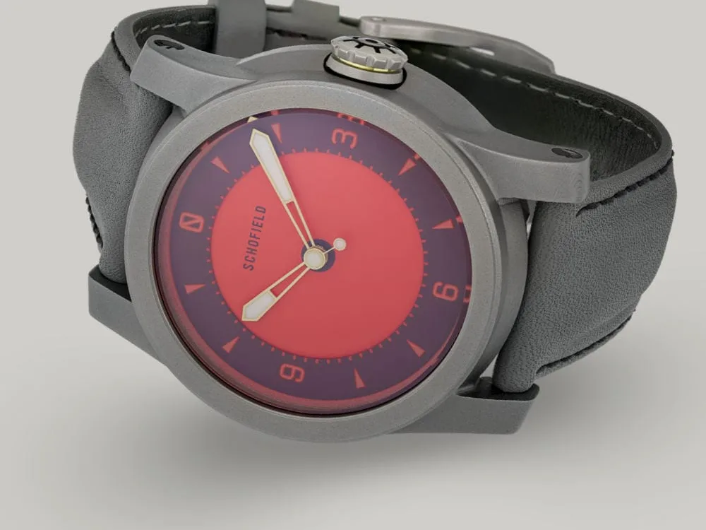 A grey titanium wristwatch with a red dial from Schofield. The Strange Lights ✦ NQR features custom lume on the Not Quite Red dial. Shown here on a grey strap with black stitching.
