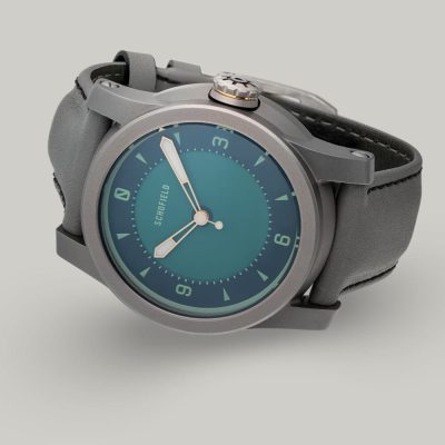 A grey titanium wristwatch with a green dial. The Strange Lights - NQR features custom lume on the Not Quite Green dial. Limited edition of 29 watches.