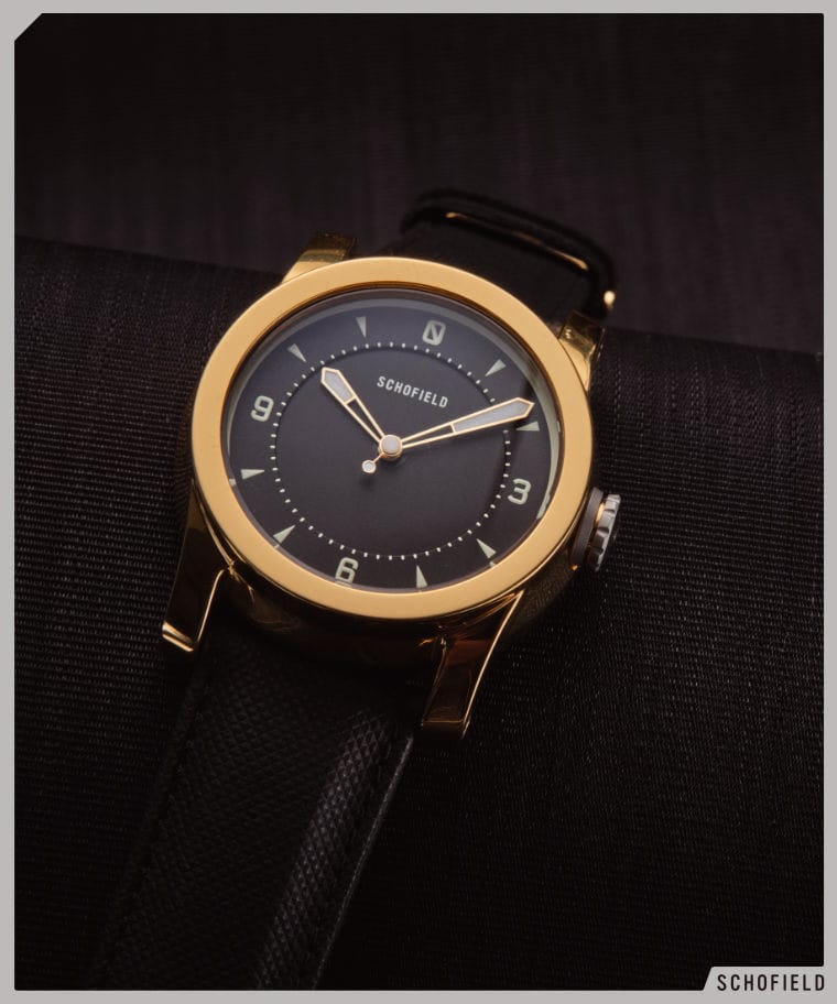 A gold Schofield watch with a black dial and simple minimal design
