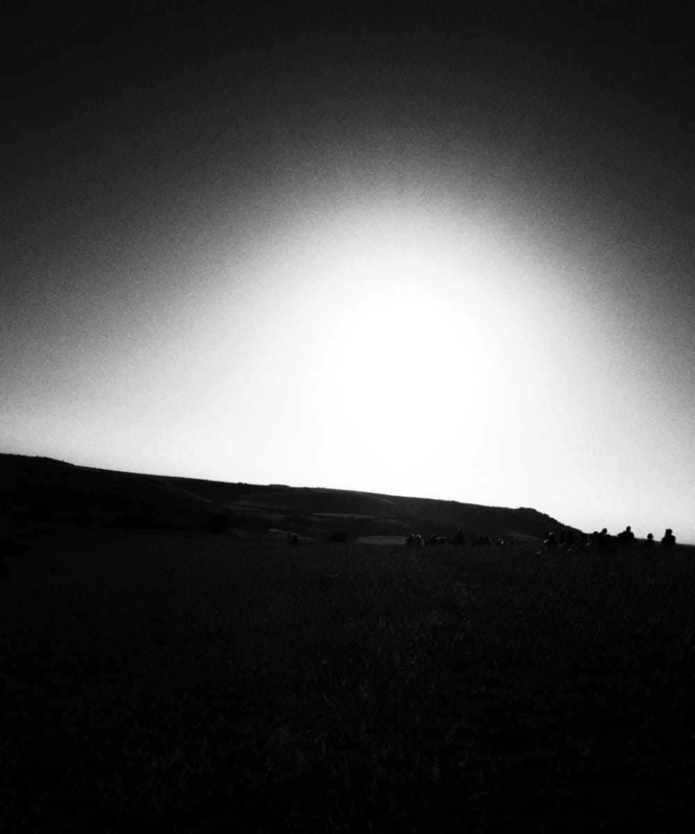 Stylized, grainy, black-and-white image of people watching the solar eclipse on the South Downs, 2026